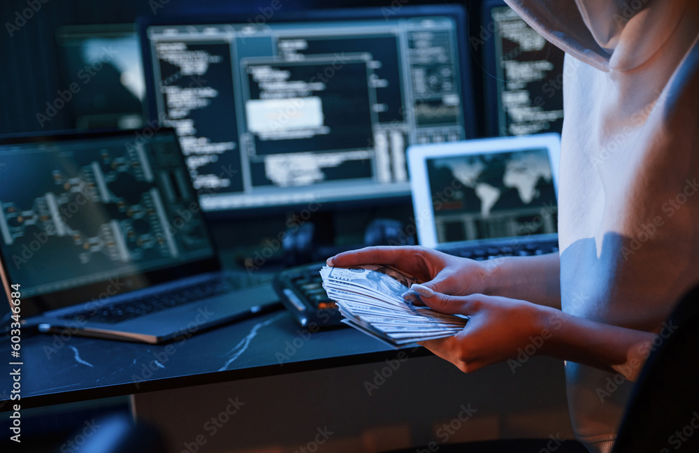 Poster with currency in hands. young professional female hacker is indoors by computer with lot of informat