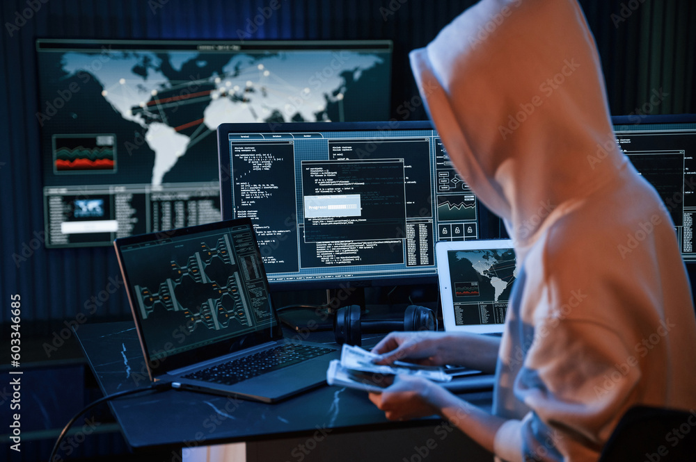 Poster with currency in hands. young professional female hacker is indoors by computer with lot of informat