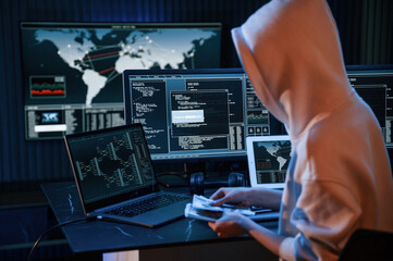 With currency in hands. Young professional female hacker is indoors by computer with lot of information on displays