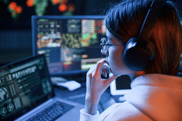 Focused on work. Young professional female hacker is indoors by computer with lot of information on...