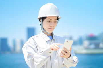 スマートフォンを手にする作業服姿の女性