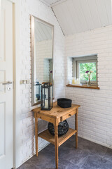 Entrance hall with white stone wall and small window, with wooden side table, mirror and decoration