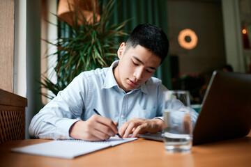 Portrait with one handsome, focused man, student, graduate in shirt preparing for entrance, studying while sitting in cafe. Concept of education, freelance work