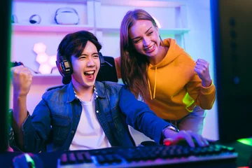 Fotobehang Gaming An Asian male gamer and Caucasian woman coach advice and discuss together in front of the gaming table. Gamer winning an esports game with a mentor. The player rejoices in victory in the competition.  © artitwpd