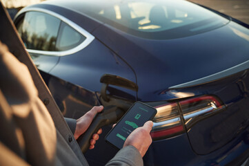Mobile app with charging data. Man is standing near his electric car outdoors