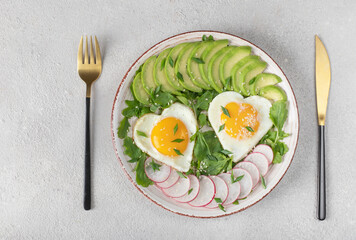 Healthy romantic breakfast - heart-shaped fried eggs served with avocado and radish, View from above
