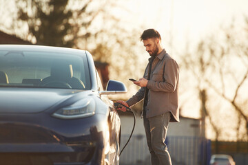 Conception of green energy. Man is standing near his electric car outdoors
