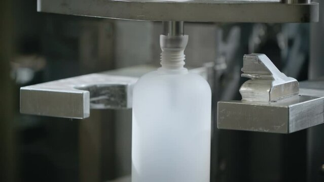 Plastic blow molding machine operating at the production factory. Blow molding machine shaping the white raw material into the bottles. Blow molding machine producing the plastic bottles.