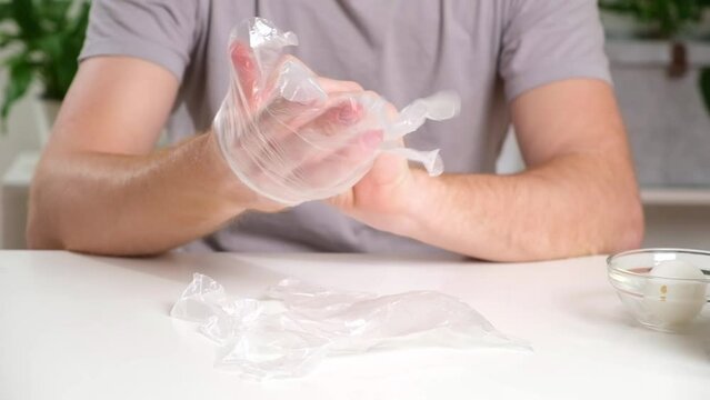A man puts disposable plastic transparent gloves on his hands to dye Easter eggs. Coloring of Easter eggs.