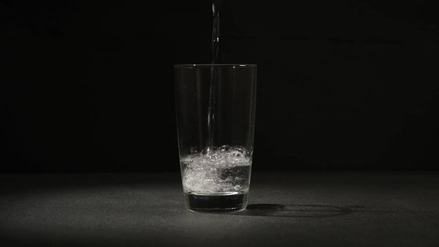 Clean drinking water is poured into a glass glass on a black background.