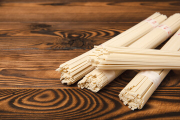 Rice noodles on a brown textured wooden background. Raw funchose noodles and rice groats. Thai dried rice noodles. Place for text. Place to copy. Close-up.