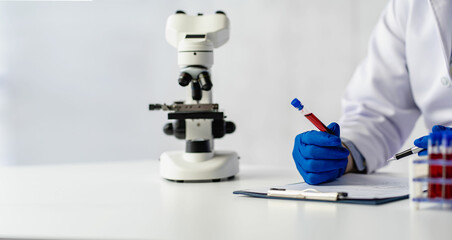 Doctor holding blood vessels for analysis and checking blood in research laboratory blood sample from rack with analyzer in lab