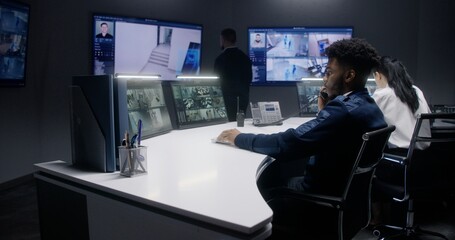 Multi ethnic security operators control CCTV cameras with AI facial scanning in police surveillance...