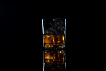 glass of whiskey with ice on a black background with reflection