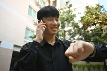 Young businessman talking on phone and looking at wrist watch To schedule a time for business negotiations.