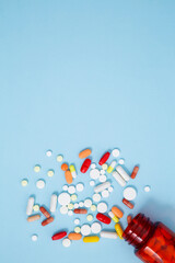 Orange bottle container with various colorful medication tablets and capsules on blue background. Concept of healthcare and medicine. Top view, copy space