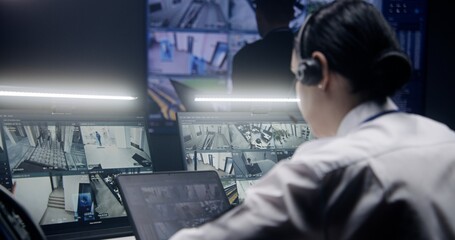 Female operator in headset zooms and monitors security cameras with AI facial recognition, uses...