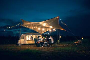 Asian LGBTQ+ couple drinking and barbecue in a romantic camping setting. Groups of friends and couples having a drink party in a camping atmosphere amidst forests and rivers.