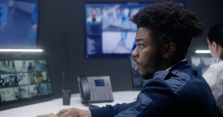 African American officer controls CCTV cameras with AI face scanning in police monitoring room....