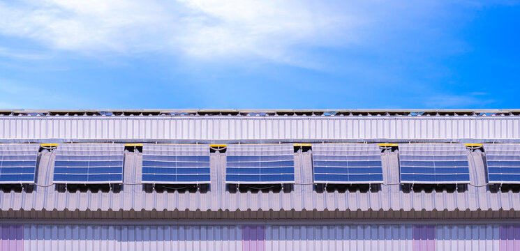 Solar Photovoltaic Panels on Corrugated Metal Roof of Factory Building against blue sky background in Panoramic view