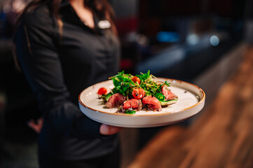 Waiter holds a plate with meat salad in the restaurant