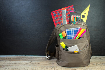 Backpack with different colorful stationery on table. Black background. Back to school.