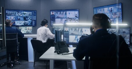 Diverse team of officers watch CCTV cameras with AI facial recognition. Employees work in security control center. Computer monitors and big digital screens showing surveillance cameras video footage.