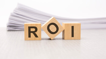 wooden block with text ROI - acronym - RETURN ON INVESTMENT. wooden blocks are on the paper white background, business concept. front view.