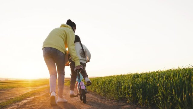 mother teaches her little daughter ride bicycle forest park sunset. happy family chidhood dream. concept two-wheeled bicycle. little daughter rides bike for first time park glare sunlight. happy