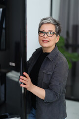 Portrait of a cheerful mature woman near the refrigerator in the home interior.