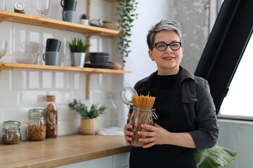 Smiling senior woman holding raw spaghetti in her hands at home kitchen.
