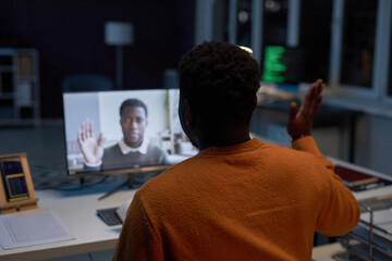 Rear view of businessman having online meeting with his colleague while working till late night in office
