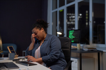 Exhausted woman sitting at her workplace with computer, she working till late night in office