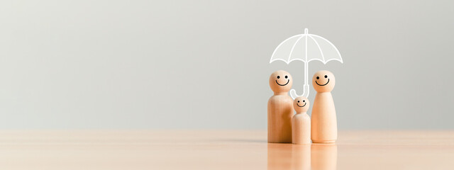 Happy family under the umbrella on raining wooden figurine model on table top background. People...