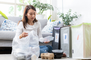 Asian young female sitting at home separating paper and plastic waste. Garbage sorting for recycle....