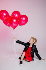 Stylish girl smiles toothlessly, wears a black leather jacket and balloons, has fun with her best friends, isolated on a pink background. Children, holiday concept, birthday.