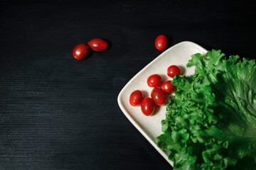 fresh green lettuce leaves and small red cherry cocktail tomatoes on black wooden background