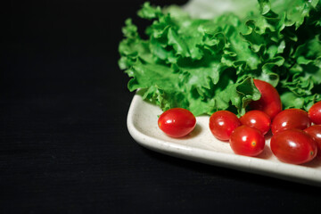 fresh green lettuce leaves and small red cherry cocktail tomatoes on black wooden background