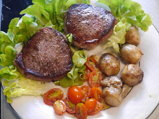 Close-up of a plate of raw, semi-cooked beef steak and a side dish of carrots, tomatoes, on a plain white plate Suitable for making menus in restaurants