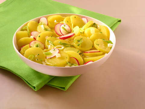 Kartoffelsalat mit Radieschen Essig und Oel in weisser Porzellanschale mit gruener Serviette