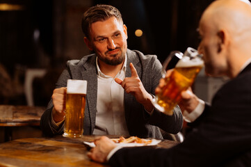 two adult friends talking while sitting in a pub. Two men drink draft beer, celebrate meeting and talk after work