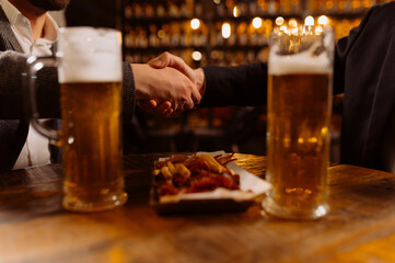 two glasses of beer on the table, greeting friends by the hand, evening in the pub, close-up