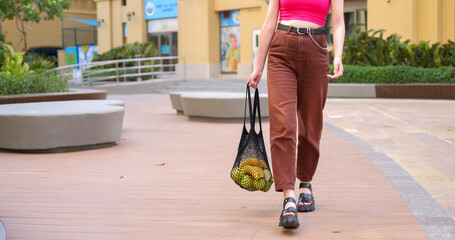 Teen girl walks with eco-friendly reusable shopping bags filled with fruits. 