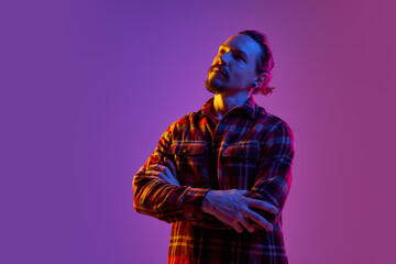 Portrait of thoughtful man in checkered shirt generating creative ideas against purple studio...