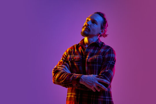 Portrait Of Thoughtful Man In Checkered Shirt Generating Creative Ideas Against Purple Studio Background In Neon Light. Concept Of Human Emotions, Facial Expression, Lifestyle