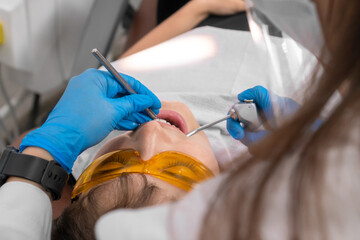 Close-up of the dentist's hands when examining the oral cavity of a young woman with a mirror and a device that supplies air and water. Concept of dentistry, medicine