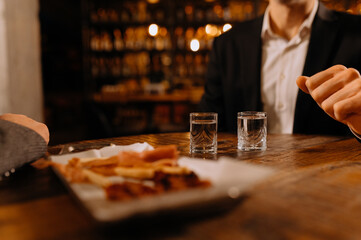 friends drink vodka and eat snacks on a wooden background. alcohol and snacks on the table. drink tequila