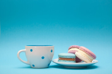 Different macarons cakes and cup of tea or coffee on blue color background with copy space, dessert and sweet food