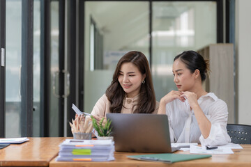 Two Young Asian businesswomen discuss with new startup project Idea presentation and analyze planning and financial statistics and investment market at an office.
