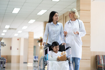 Fototapeta premium Female pediatrician doctor and child patient on wheelchair with her mother in the health medical center